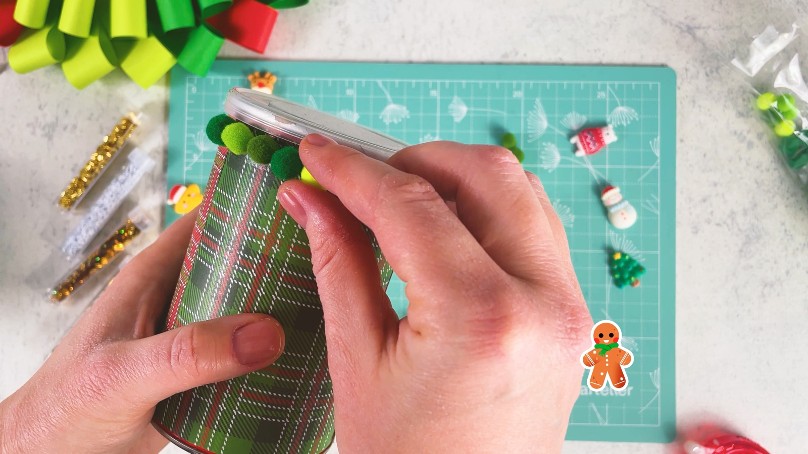 Pressing a row of green pom-poms onto the tape around the top of the can