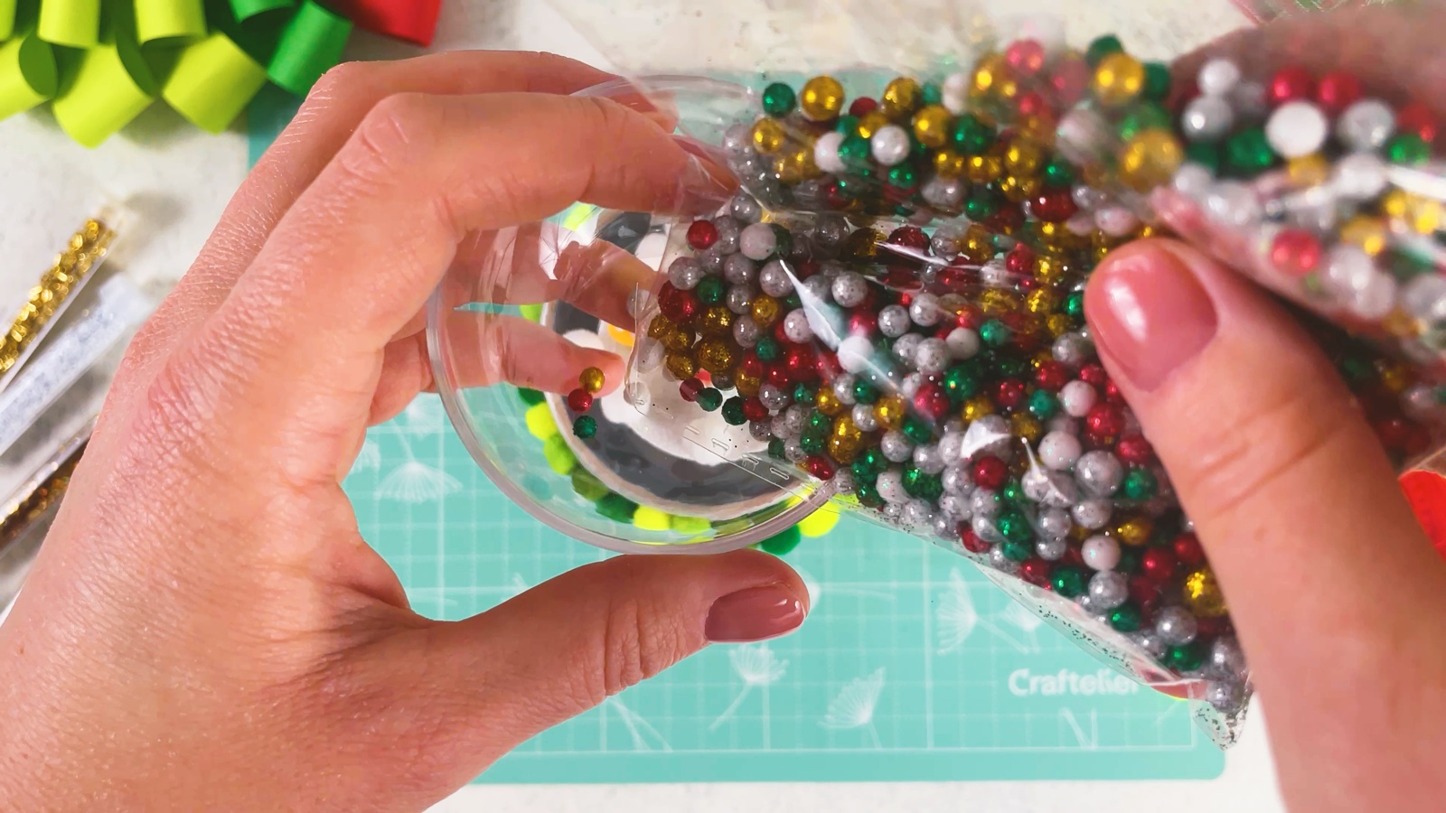 Pouring red, green, gold and white beads into the bauble half
