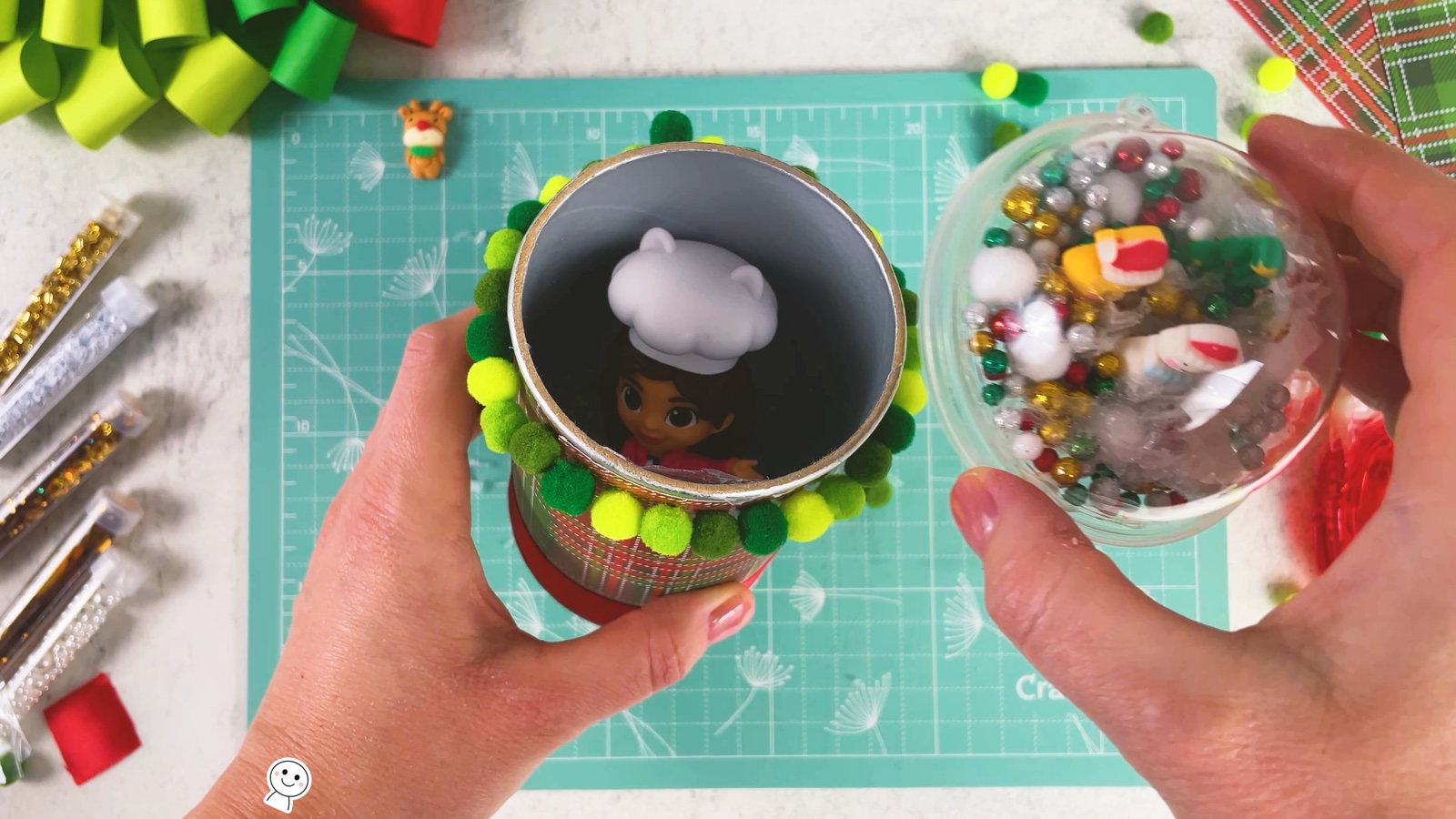 The open can with a small doll in a chef hat hidden inside, the snow globe lid held next to it