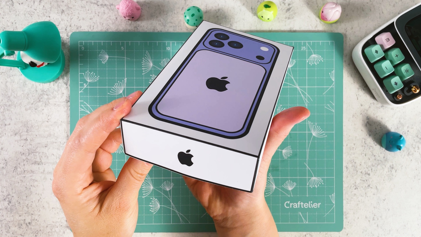 The closed iPhone box with the purple phone on the lid and an Apple logo on the side