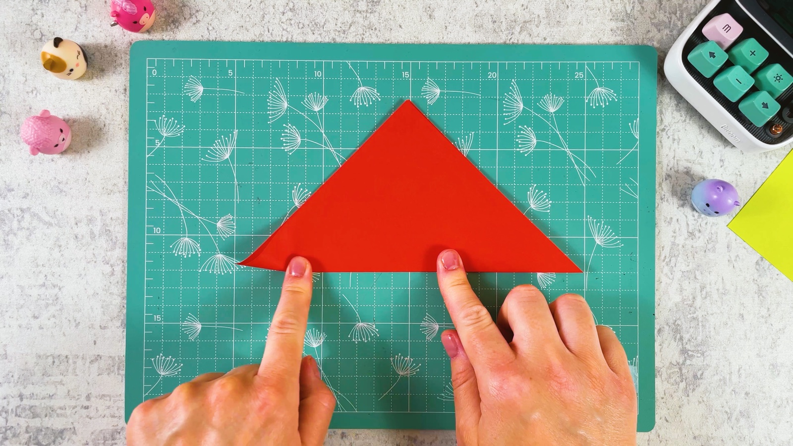 Pressing a crease into a red paper square folded into a triangle