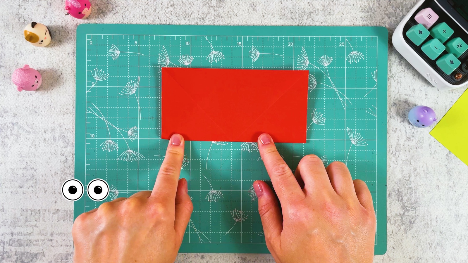 Red paper folded in half into a rectangle, fingers pressing the fold