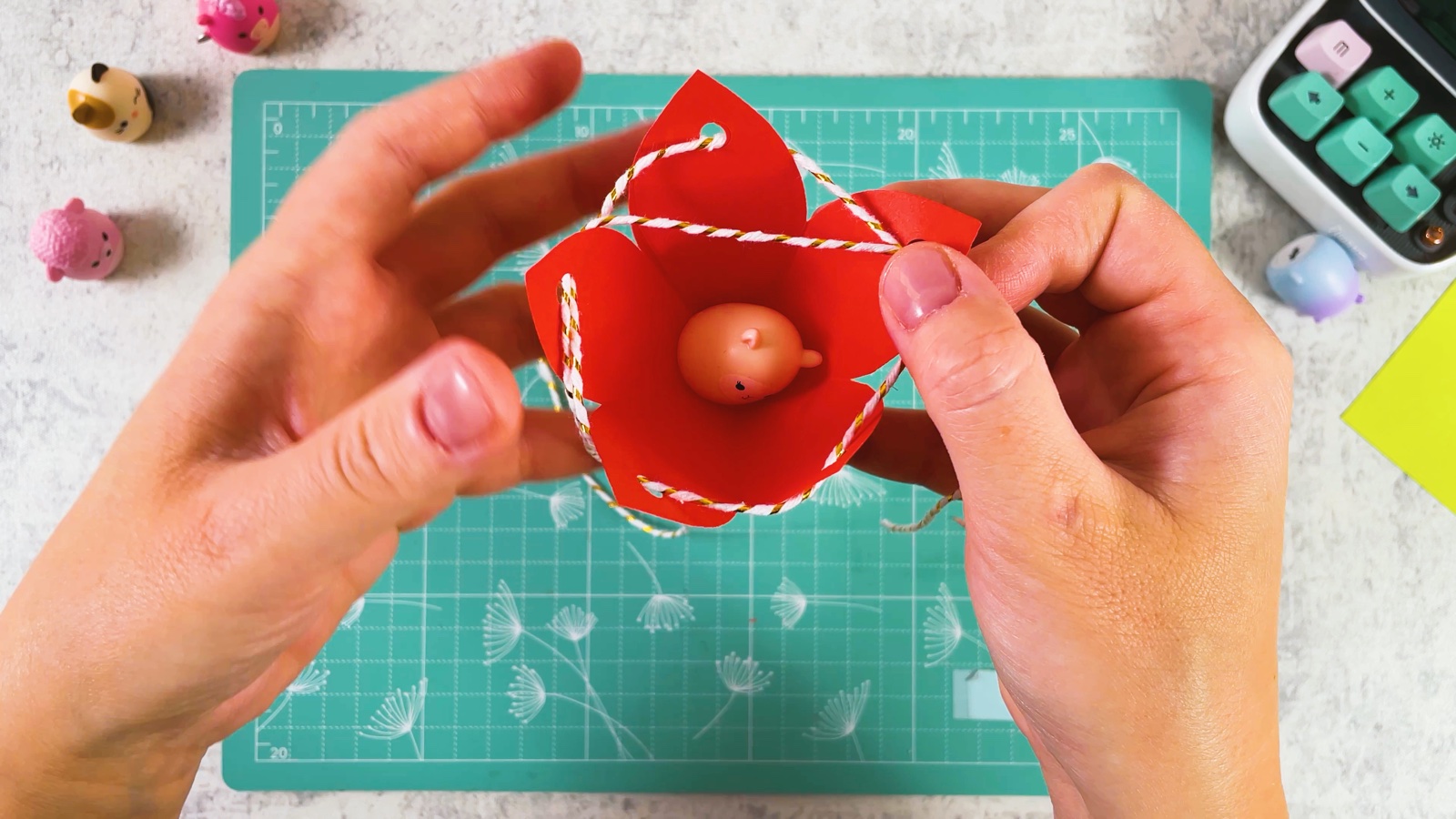 A tiny toy sitting inside the open red paper cup with the string around the petals