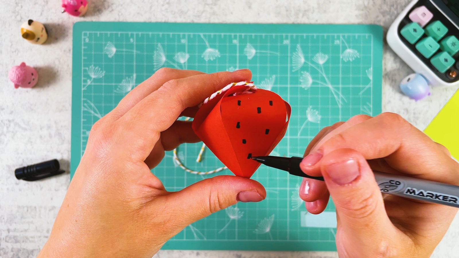 Drawing small black seeds on the closed red paper strawberry with a marker
