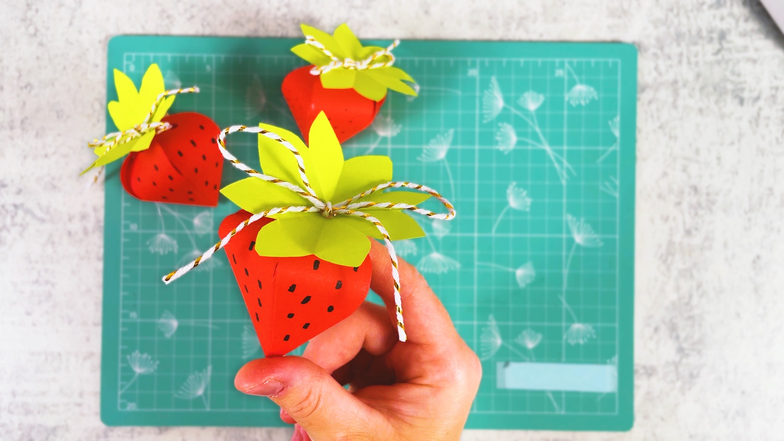 Two finished paper strawberry gift boxes with green leaves and string bows