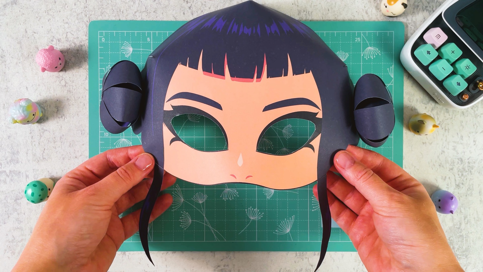 The finished paper Zoey mask with dark hair, two round buns and two thin strands hanging past the chin
